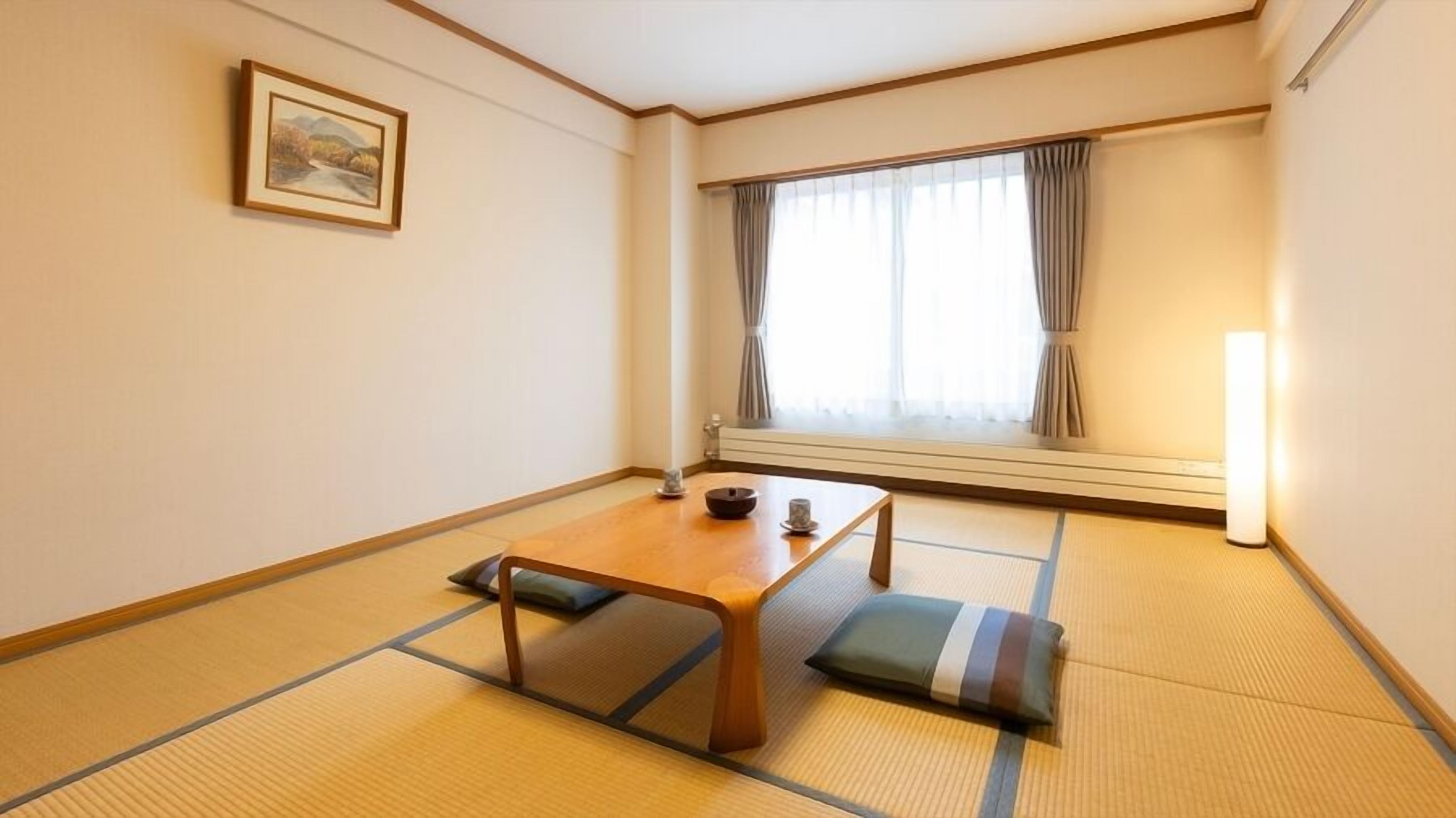 Una habitación japonesa tradicional con suelo de tatami, una mesa de madera baja, un cojín, un cuadro en la pared y una ventana con cortinas.