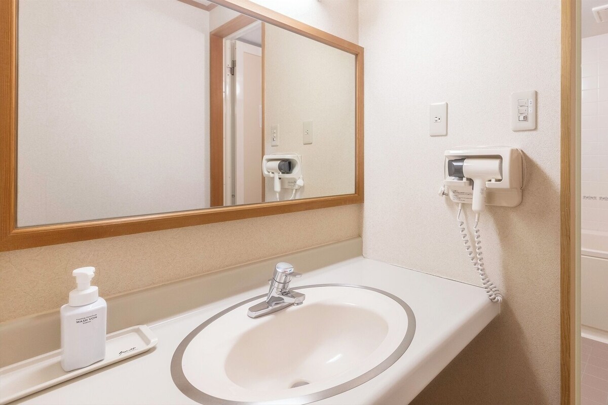 A bathroom with a sink, mirror, and a hairdryer on a wall-mounted outlet.