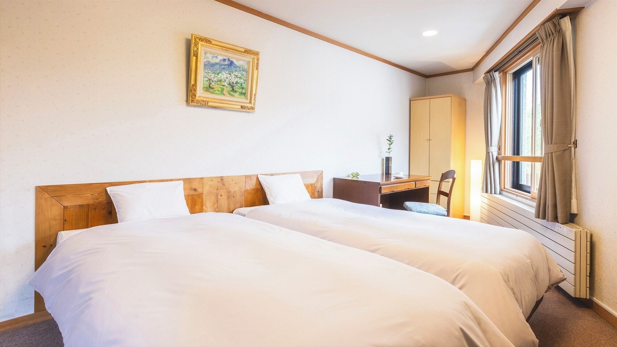 Habitación de hotel con dos camas, un escritorio, una silla, una ventana con cortinas y un cuadro en la pared.