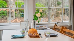 Ein Esstisch mit einer Lampe, einer Blumenvase, Brot und Gläsern.
