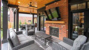 Une terrasse extérieure aménagée avec des meubles en osier, une cheminée et un téléviseur.
