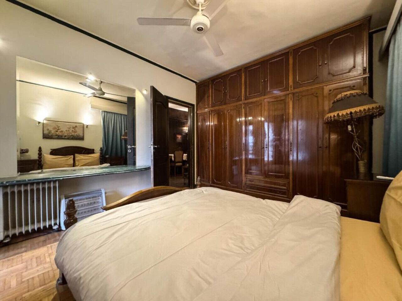 A hotel room with a large bed, wooden paneling, a ceiling fan, a mirror, and a radiator.
