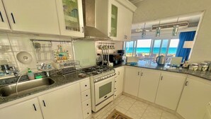 Una cocina con armarios blancos, estufa a gas y vista al océano.