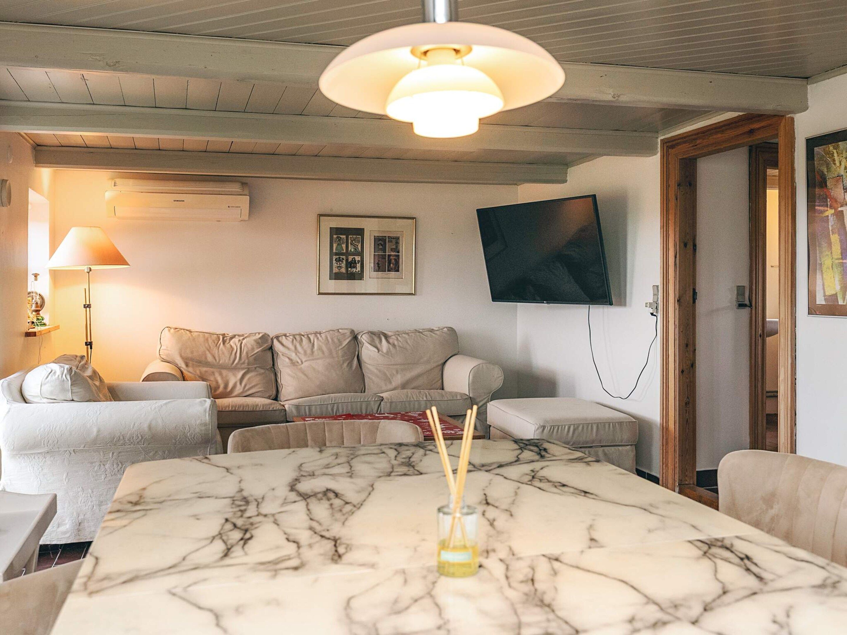 A living room with a marble table, a sofa, a TV mounted on the wall, and a lamp.