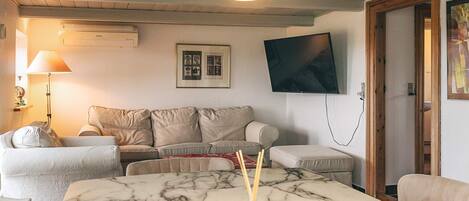 A living room with a marble table, a sofa, a TV mounted on the wall, and a lamp.