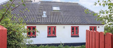 A white building with a grey roof, red windows, and a red fence.