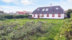 A white house with red windows and a sloped roof, surrounded by greenery and other houses. - 5 Person Holiday Home in Veslos (Vesløs)