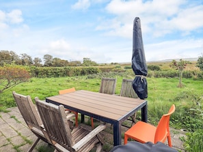 Un espace de restauration en plein air avec une table et des chaises, un parasol et une vue sur un champ verdoyant et des arbres.