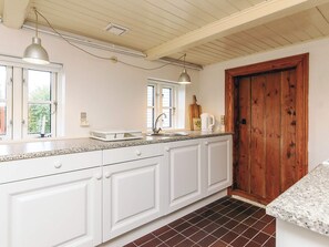 A kitchen with white cabinets, a wooden door, and a window with a view of greenery. - 5 Person Holiday Home in Veslos (Vesløs)