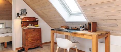 A cozy attic bedroom with a sloped ceiling, a skylight, a wooden desk, a white chair, and a vintage dresser.