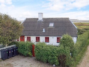 Une maison blanche avec des portes et des fenêtres rouges, un toit gris et une petite fenêtre à l’étage supérieur.