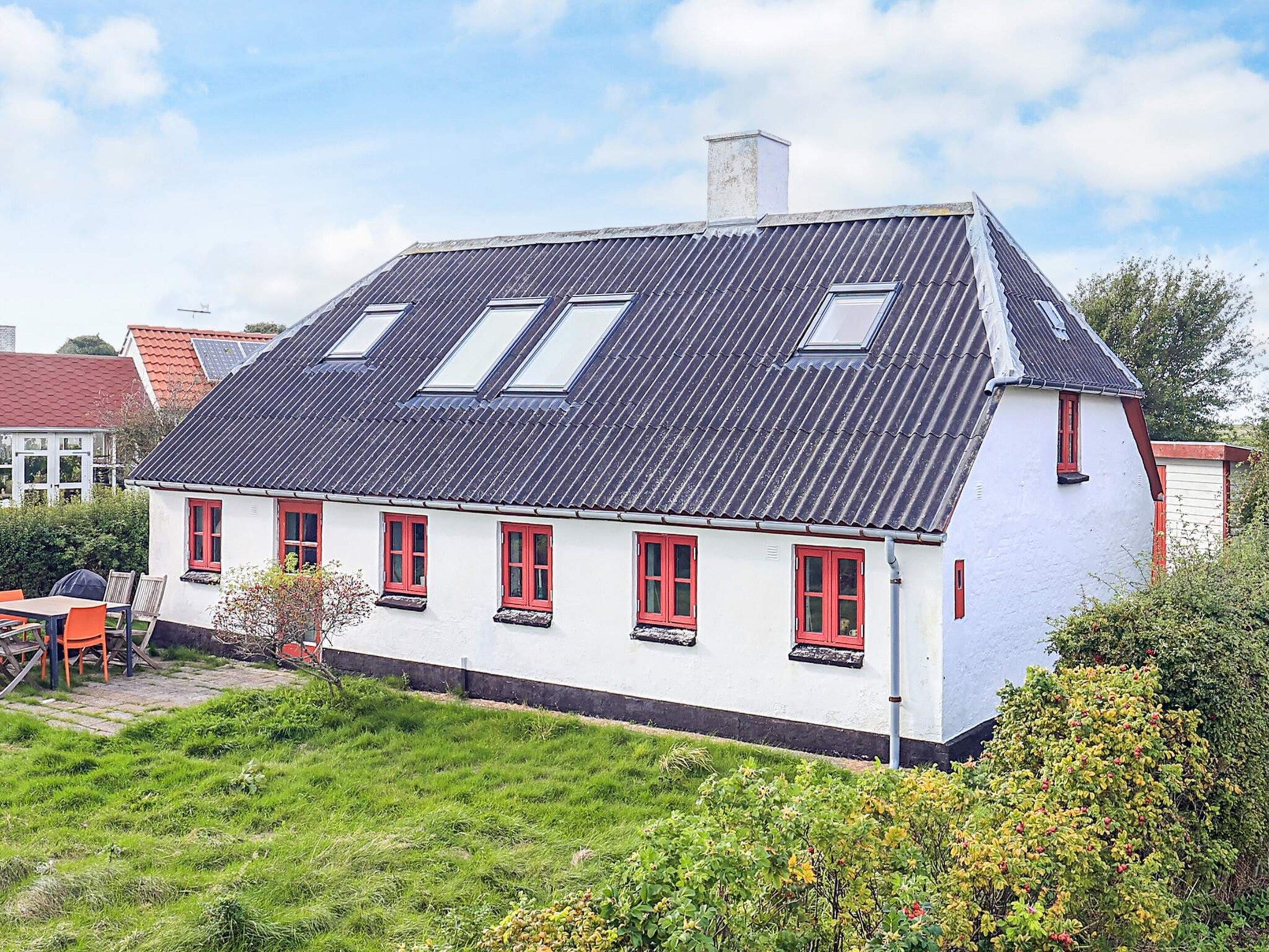 Ett vitt hus med röda fönster och ett sluttande tak.
