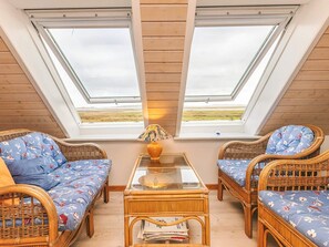 Una habitación acogedora con dos ventanas amplias, muebles de mimbre y una mesa de vidrio.
