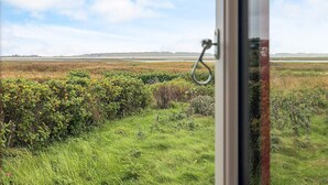 A view through a window with a metal handle, a grassy field, and a distant horizon. - 5 Person Holiday Home in Veslos (Vesløs)