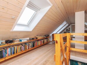 A spacious attic room with wooden floors and slanted ceilings, featuring skylights and wooden bookshelves filled with books. - 5 Person Holiday Home in Veslos (Vesløs)