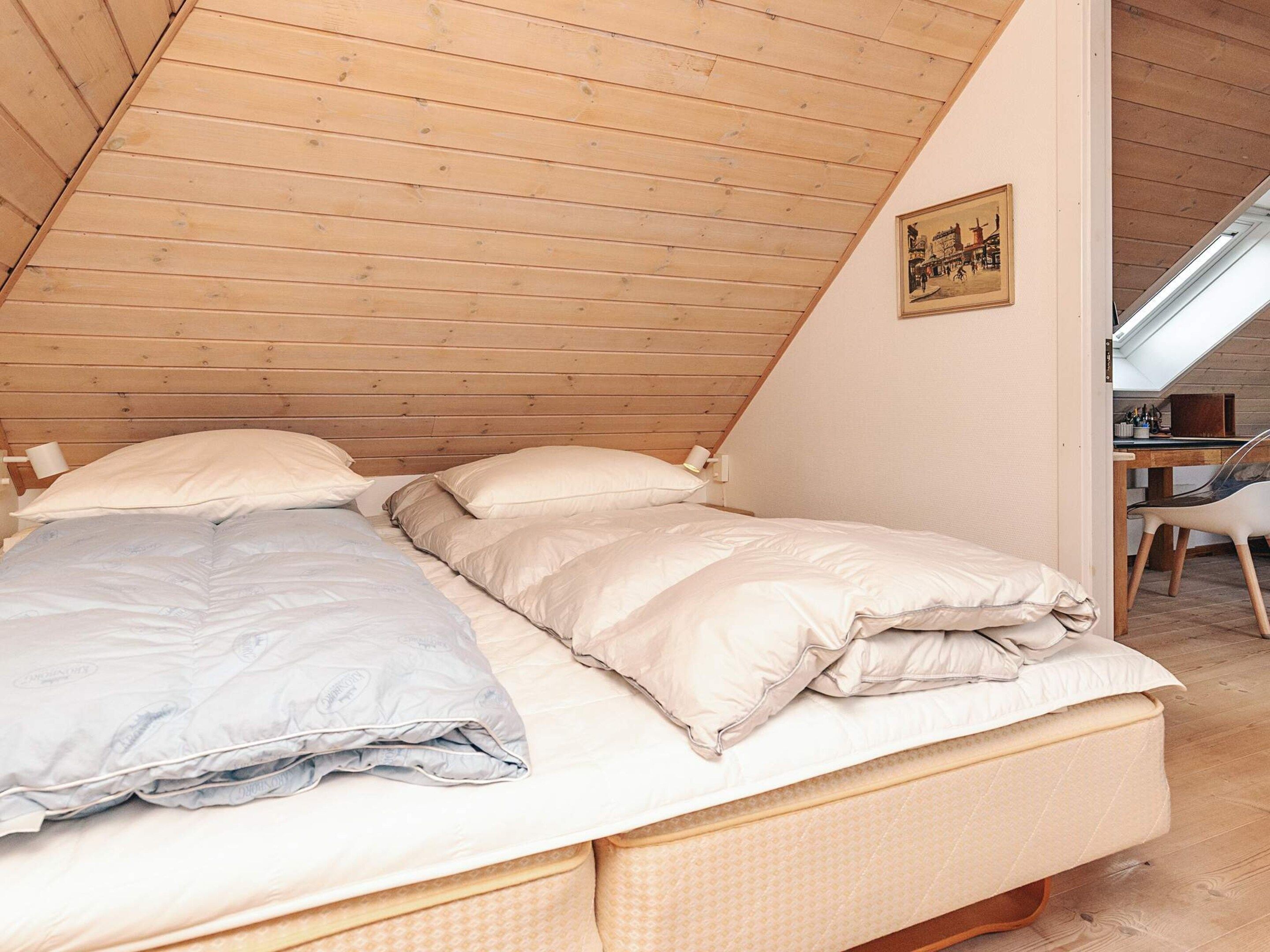 A cozy bedroom with a sloped ceiling, a bed with white bedding, and a small desk with a chair.