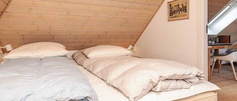 A cozy bedroom with a sloped ceiling, a bed with white bedding, and a small desk with a chair.