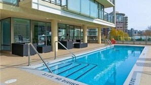 Ein Schwimmbecken mit Stufen, umgeben von einem Gebäude mit Balkonen und Terrassenmöbeln.
