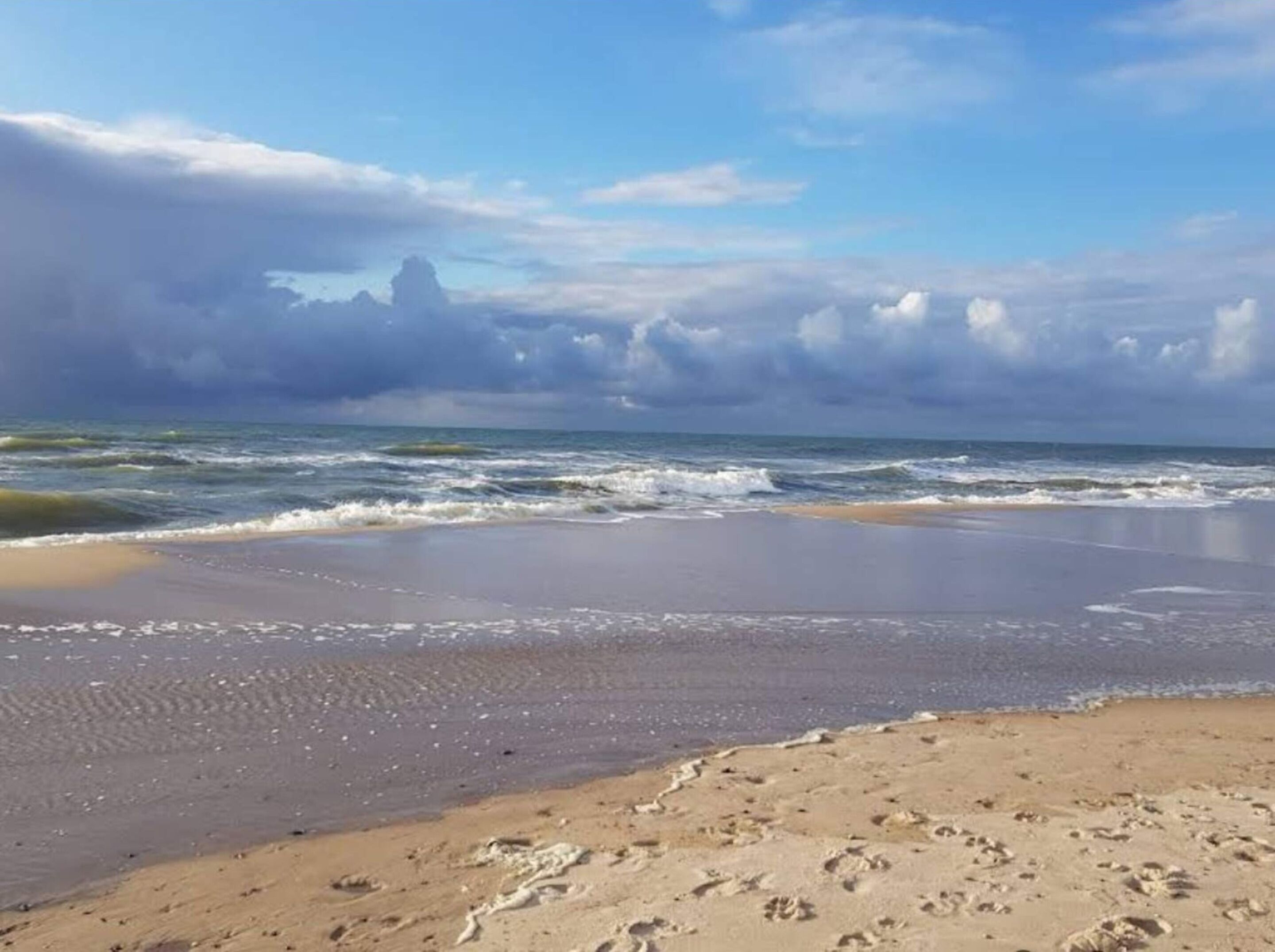 A beach with footprints in the sand, waves, and a cloudy sky.