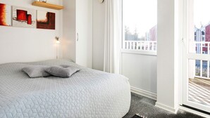 A bedroom with a large bed, a window with a view of a building, and artwork on the wall.