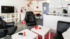 A modern living room with a flat-screen TV, leather chairs, a small table, and a red and white flag decoration.