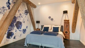 Une chambre à coucher avec un lit, des poutres en bois, un mur décoré de motifs floraux, deux tables de chevet et une horloge.