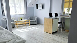 Ein modernes Hotelzimmer mit Bett, Schreibtisch, Stuhl und einer kleinen Küchenzeile.