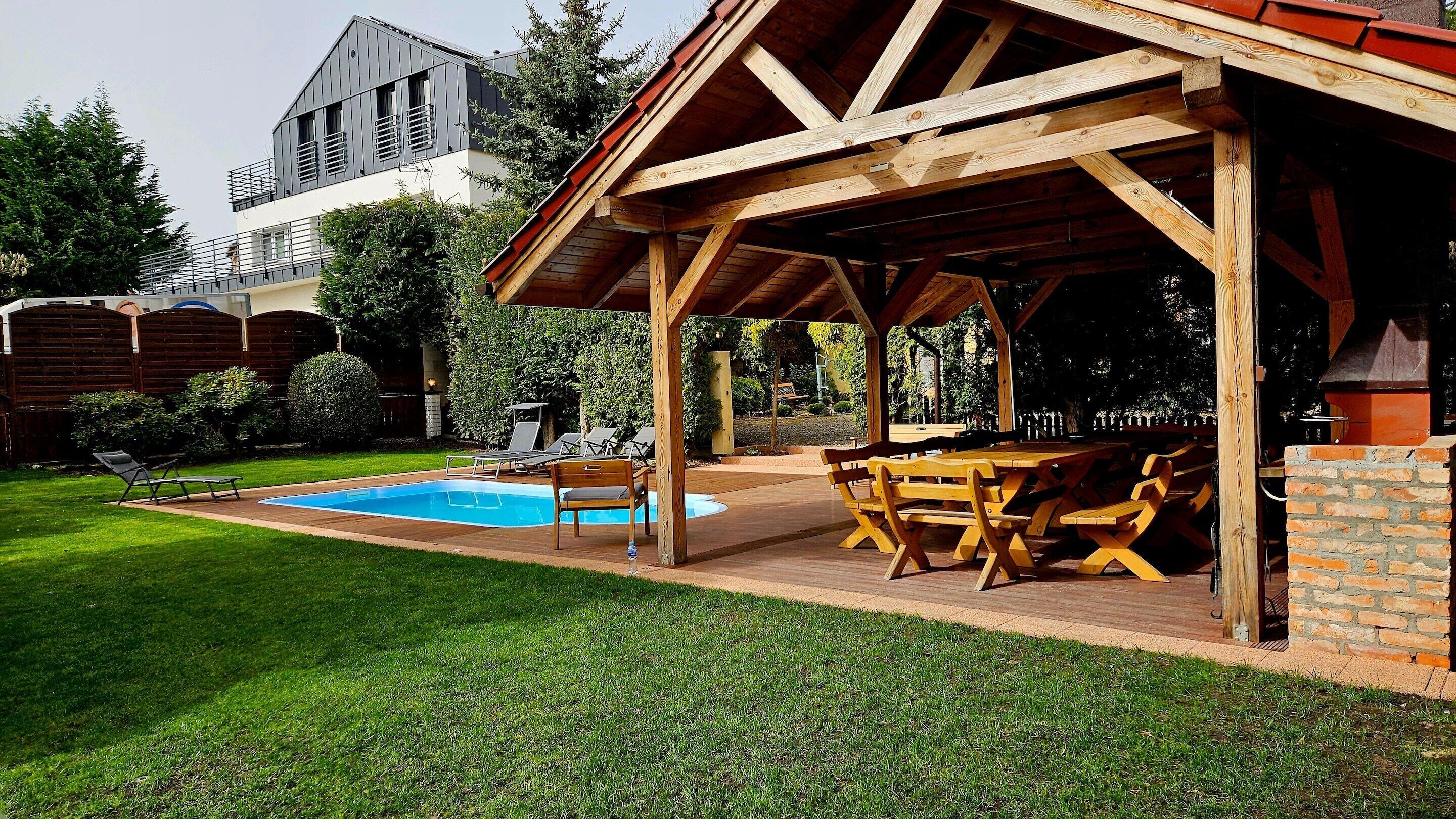 Un patio techado al aire libre con mobiliario de madera, una piscina y una zona de barbacoa.
