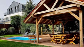 Ein überdachter Außenbereich mit Pool, Liegestühlen und einem Holztisch.