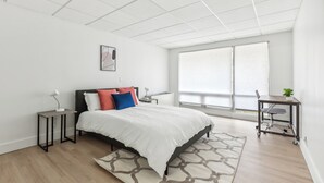 A modern bedroom with a large bed, a desk, and a view of the outdoors. - East 120 I Modern Refinished Apt Downtown I Gym (Rochester)