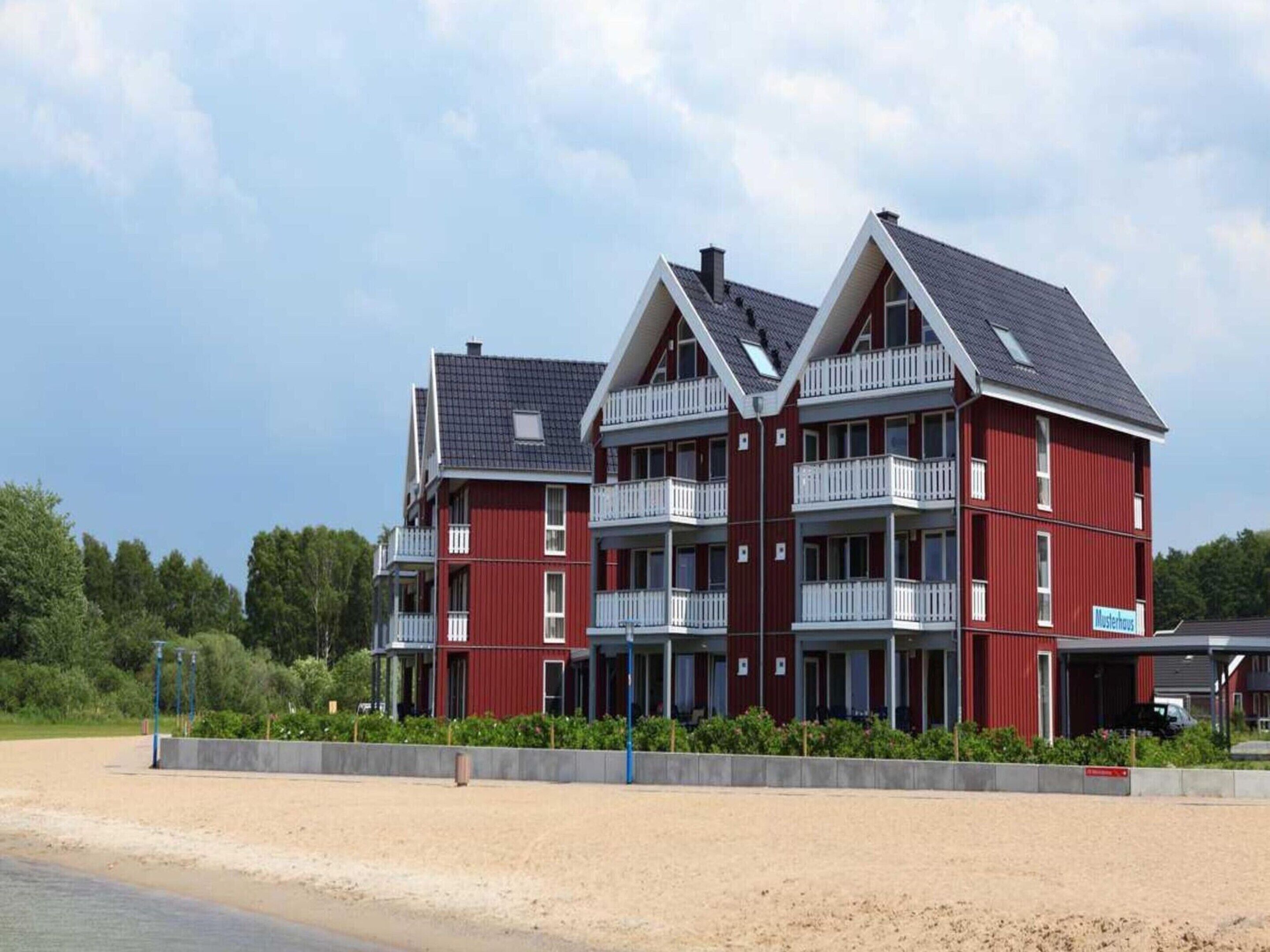Ein rotes Gebäude mit mehreren Balkonen und einer flachen Dachterrasse in Strandnähe.