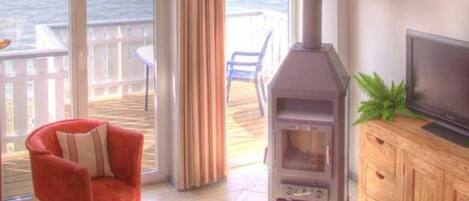 A living room with a fireplace, a TV, and a view of the ocean.