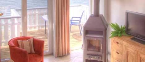 Una habitación acogedora con una silla roja, una mesa de madera, un televisor y una estufa de leña.