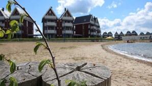 Een hotel aan het strand met traditionele architectuur, een zandstrand en een houten paal op de voorgrond.