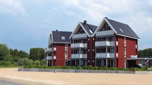 Een rood meerlaags gebouw met balkons, nabij een strand.