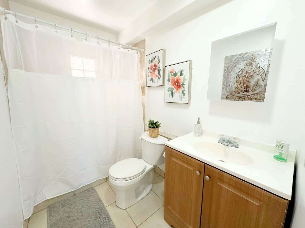 Un baño con cortina de ducha, inodoro, lavabo y armario. Hay dos obras de arte enmarcadas en la pared.