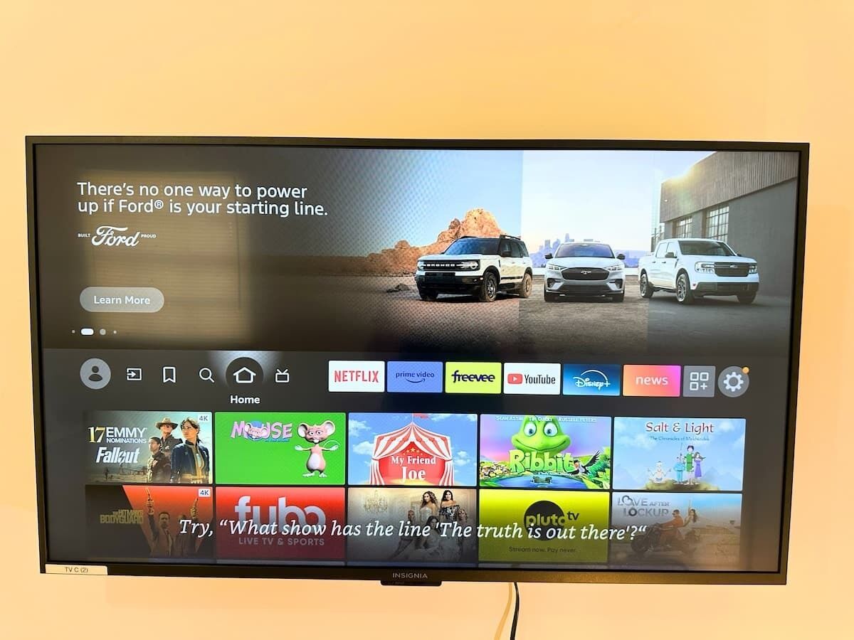 A television screen displaying a home screen with various streaming services and a promotional image for Ford vehicles.