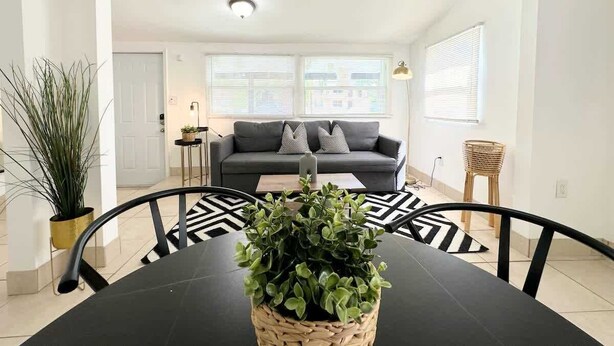 Una sala de estar moderna con una mesa de comedor negra, un sofá gris y una planta en maceta.