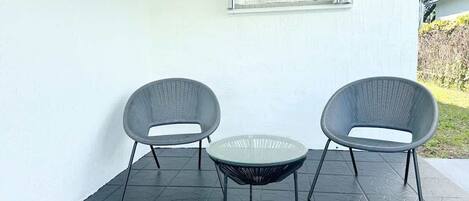 A patio area with two chairs and a small table, a window with blinds, and a notice sign about 24-hour video surveillance.