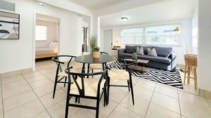 Una sala de estar moderna con una mesa de comedor redonda, sillas negras, un sofá gris y un tapete blanco y negro.