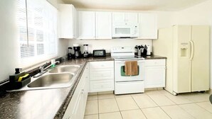 Una cocina compacta con armarios blancos, un microondas, una estufa y un refrigerador.