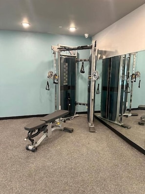Ein Fitnessraum mit einer Bank, einem Squat-Gestell und einem Spiegel.