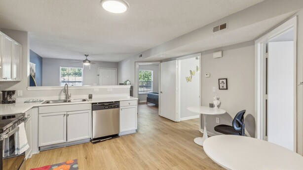 A modern kitchen with white cabinets, a dishwasher, and a dining area with a white table and chairs.