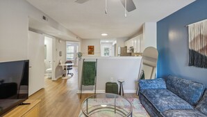 A modern living room with a flat-screen TV, a blue sofa, a glass coffee table, and a ceiling fan.