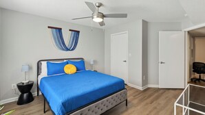 A bedroom with a bed, a ceiling fan, a nightstand, a lamp, and a door. - CB 3504-103 Fayetteville Oasis I Modern, Comfy (Fayetteville)