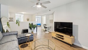 A modern living room with a grey sofa, a TV on a wooden stand, a ceiling fan, and a small round table. - CB 3504-103 Fayetteville Oasis I Modern, Comfy (Fayetteville)