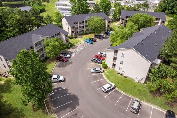 Vista aérea de un complejo residencial con varios edificios de apartamentos, un estacionamiento y zonas verdes circundantes.
