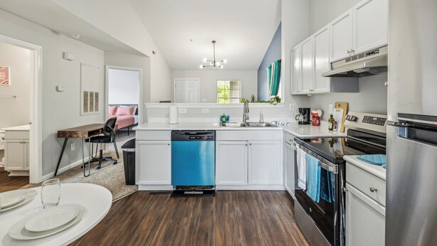 A modern kitchen with white cabinets, a blue dishwasher, stainless steel appliances, and a dining area with a round table and chairs. - CB 3508-304  Fayetteville Oasis I Modern, Comfy (Fayetteville)