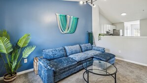 A living room with a blue wall, a blue sofa, a glass coffee table, and a potted plant. - CB 3508-304  Fayetteville Oasis I Modern, Comfy (Fayetteville)