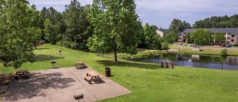 Un parque con mesas de picnic, un estanque y un edificio al fondo.